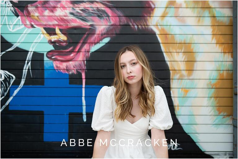 Senior picture of a girl in white dress, colorful mural as background