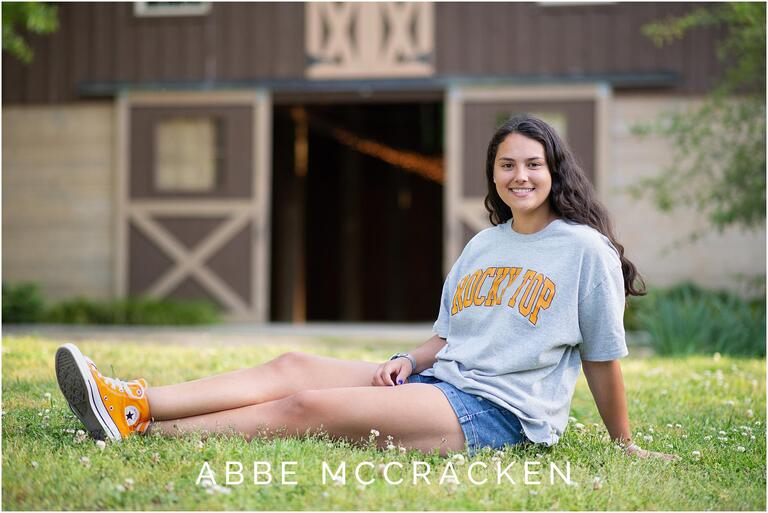 Senior portrait near barn, wearing college gear and orange Converse at Marvin Efird Park