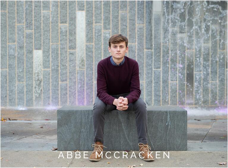 Senior portrait of boy sitting on stone in front of Romare Bearden waterfall