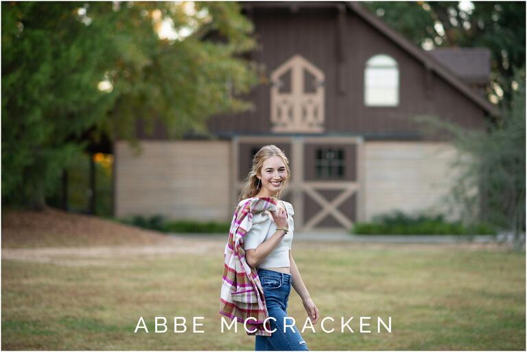 Senior girl walking across a field with plaid jacket over her shoulder