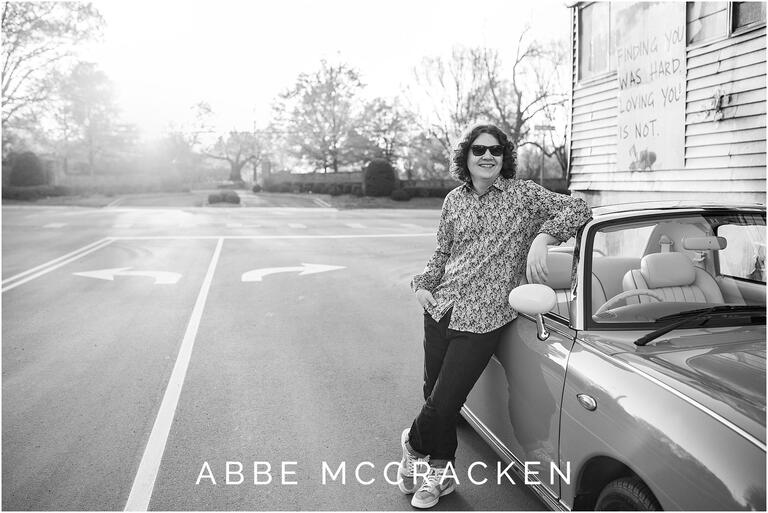 Black and white senior portrait of a boy leaning on a vintage car