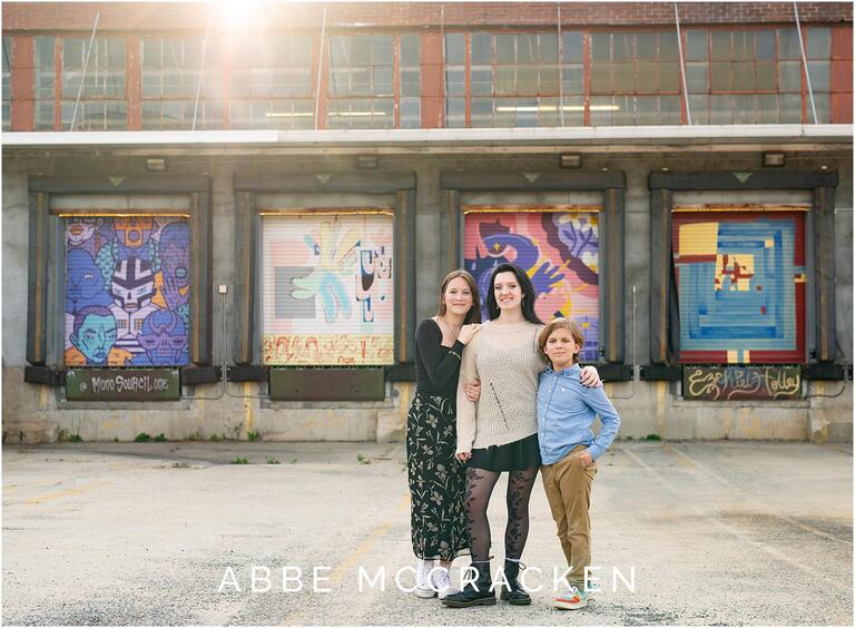 Professional family portraits in Charlotte, NC - Siblings standing in front of the Camp North End loading dock murals