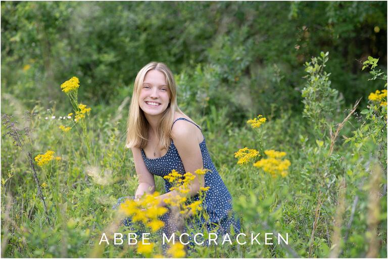 Senior portrait of a high school graduate amongst yellow flowers in a wheat field, natural setting