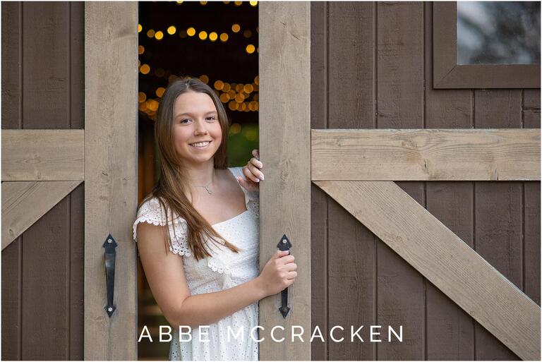 Senior portrait with girl framed by barn doors and yellow twinkling lights