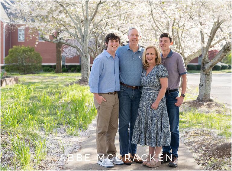 Family of four smiles in front of spring blossoms in Matthews, NC