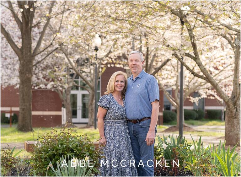 Husband and wife in downtown Matthews in front of beautiful spring trees during spring senior session 