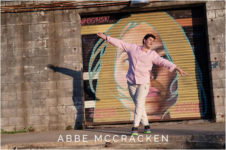 Portrait of a senior guy dancing at Camp North End in front of a colorful mural