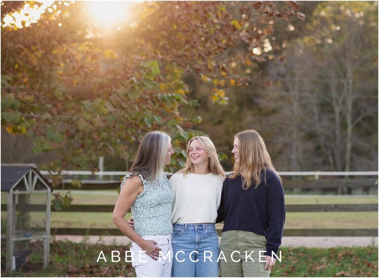 Mother and teenage daughters laughing at each other, background is the family farm