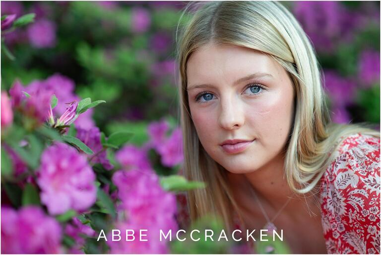 Portrait of a gorgeous blonde girl with blue eyes leaning into the blooming purple azaleas