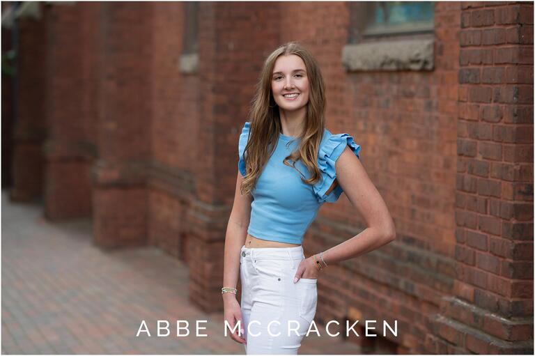 Senior portrait of a girl in blue and white standing near a red brick church in Uptown Charlotte