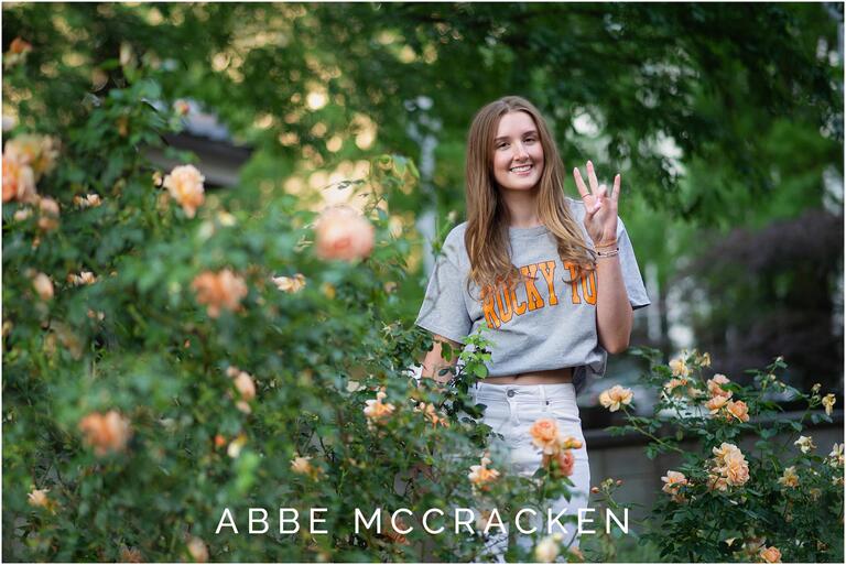 Senior portrait of a girl in Rocky Top t shirt surrounded by orange roses, photographed in Romare Bearden Park in Charlotte, NC