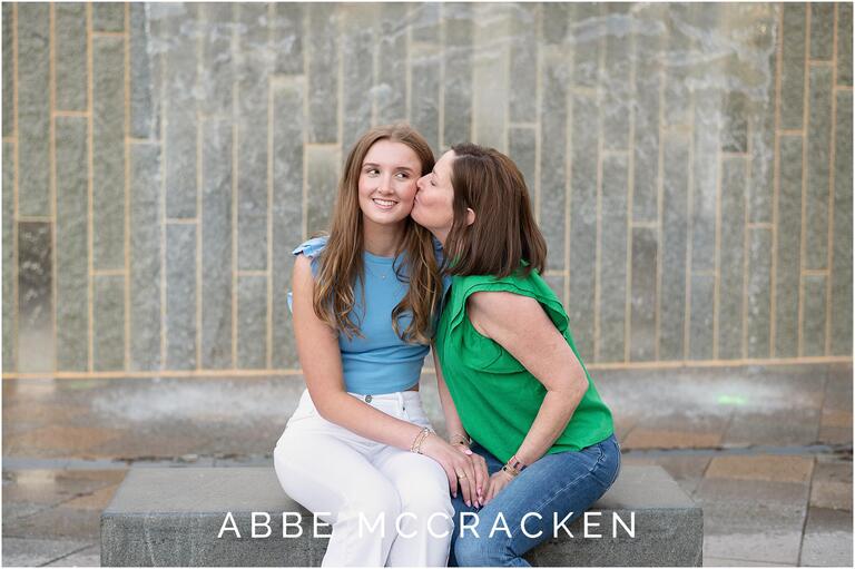 Mom kissing her high school senior daughter on the cheek, photographed in Romare Bearden Park in Charlotte NC