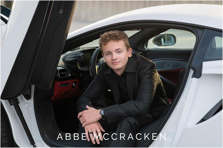 portrait of a high school senior dressed in black suit sitting in a white sports car