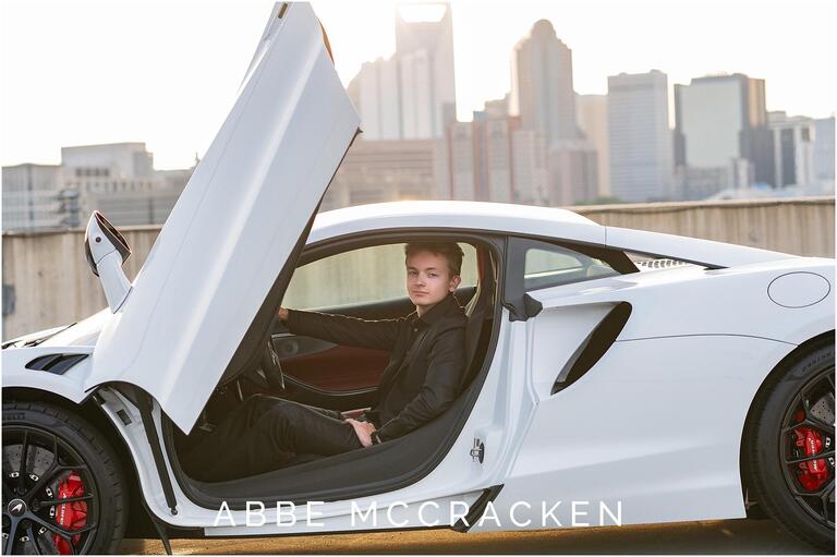 Senior portrait setting in a white sports car with Charlotte skyline in the background