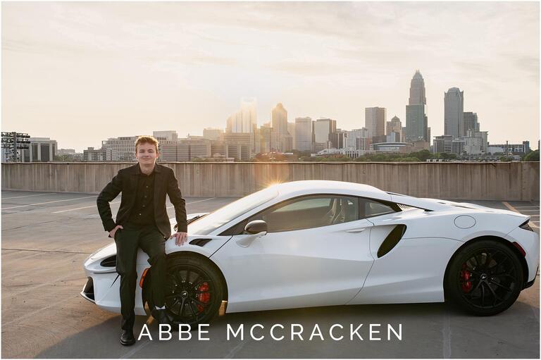Senior portrait setting on the front of a white sports car with Charlotte skyline in the background