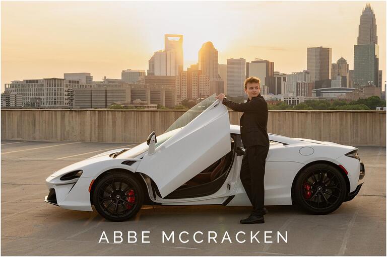 Senior portrait of a boy in all black suit getting into a white McLaren sports car as the sun sets over Uptown Charlotte, NC