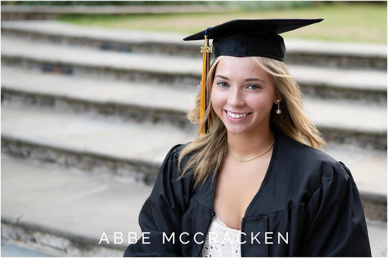 Gorgeous blond in senior gap and gown sitting on the steps of The Green in Uptown Charlotte