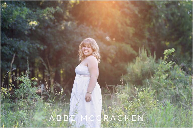 Senior portrait in a field with intense sun flare, graduate in white sun dress