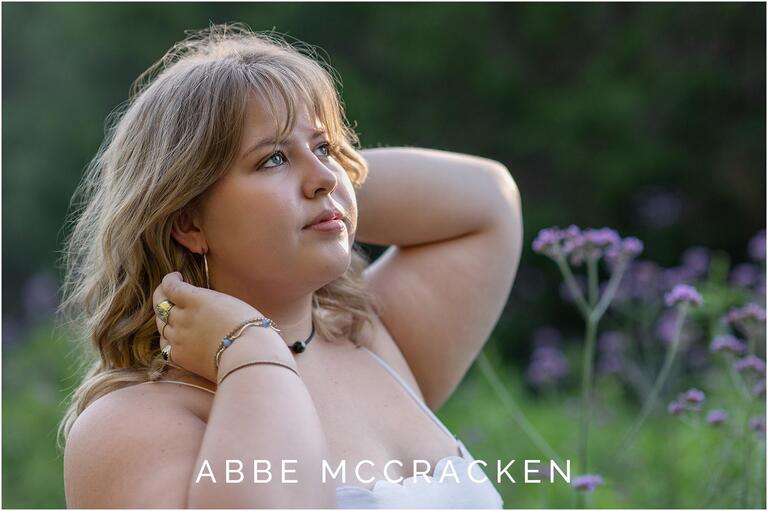 senior portrait of girl looking to the sky with purple flowers and forest as bokeh